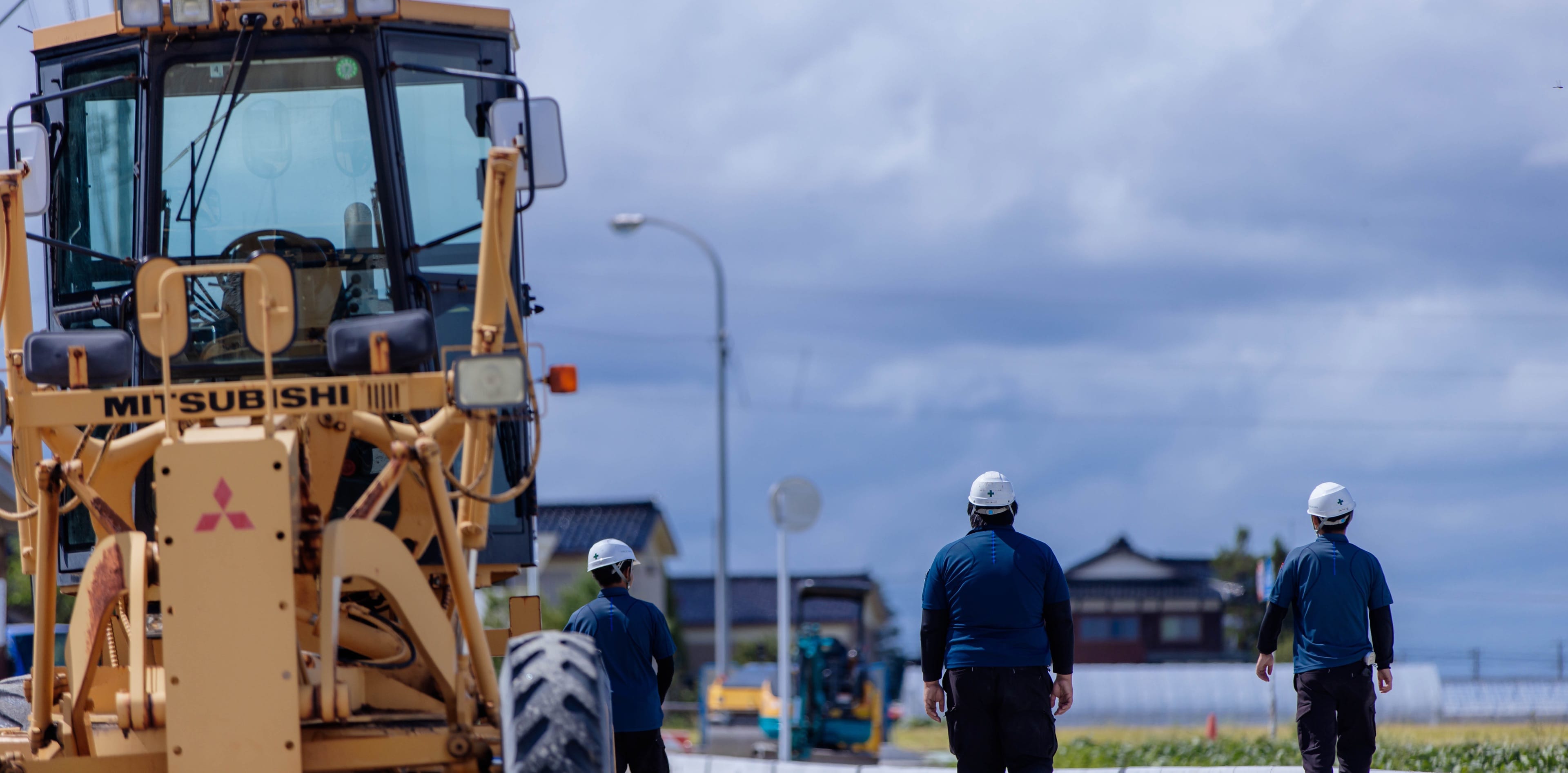 道路工事の現場を歩く作業員とグレーダー